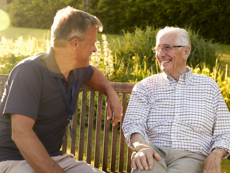 A senior man and his son talk outside on a bench