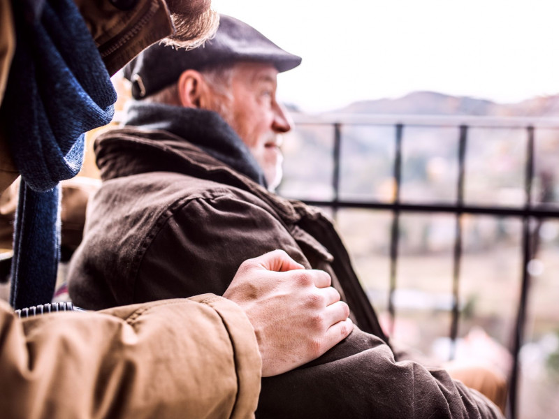 A senior man in a wheelchair and his caregiver walk on a cold day