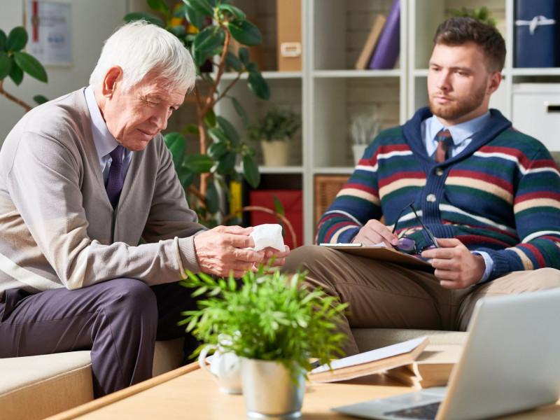 A senior man and a therapist talk together in an office