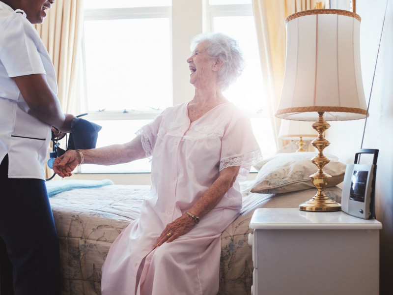 A senior woman smiles while a nurse takes her blood pressure