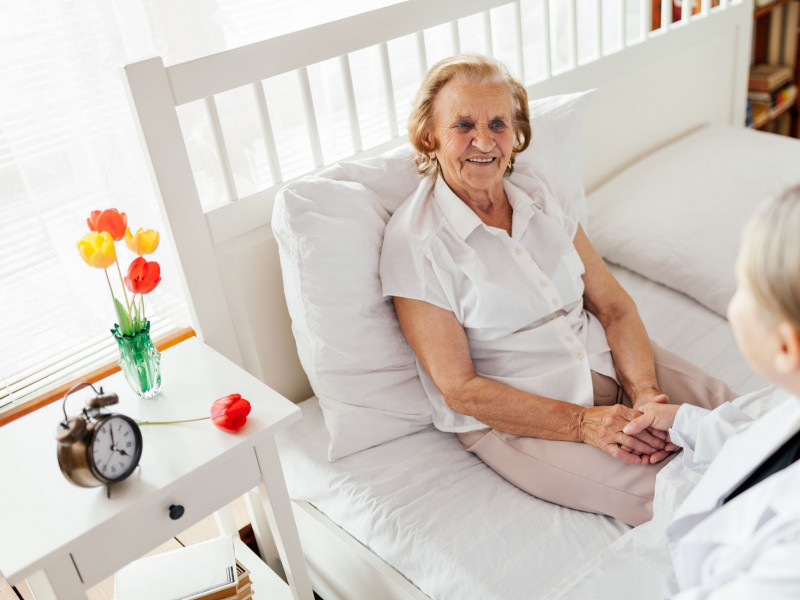 A senior woman sitting up in bed shakes hands with her doctor