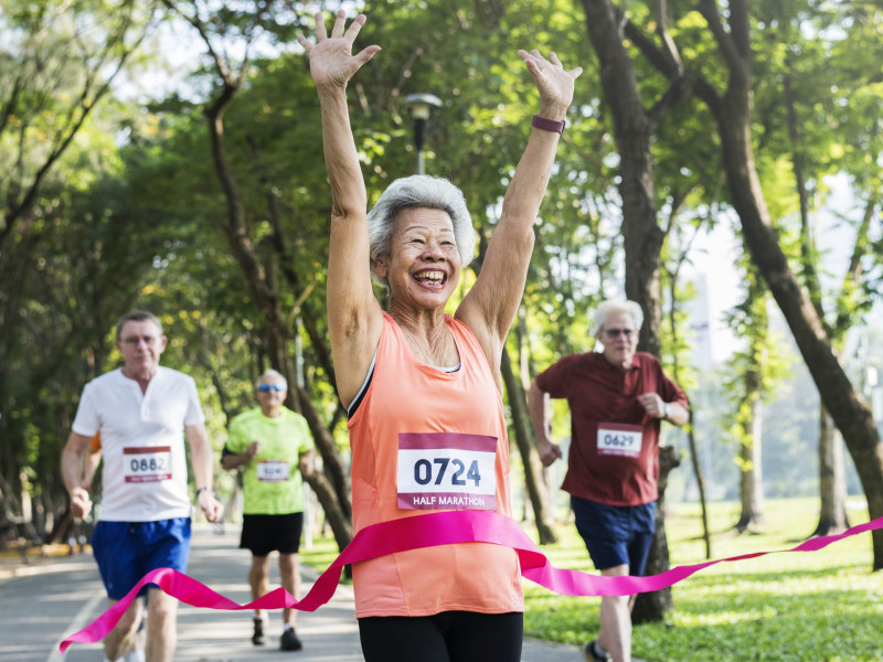 A senior woman smiles as she crosses the finish line of a race