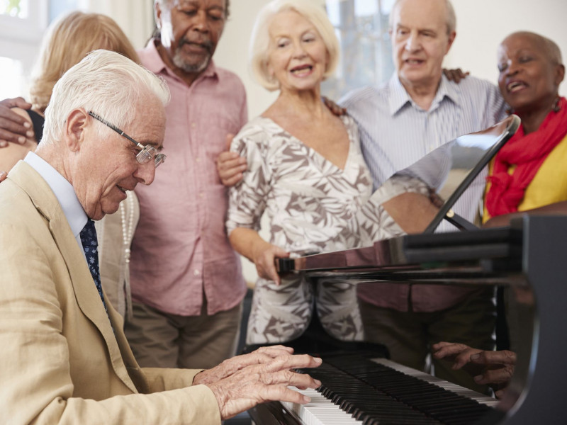 A senior man plays the piano while his friends sing along