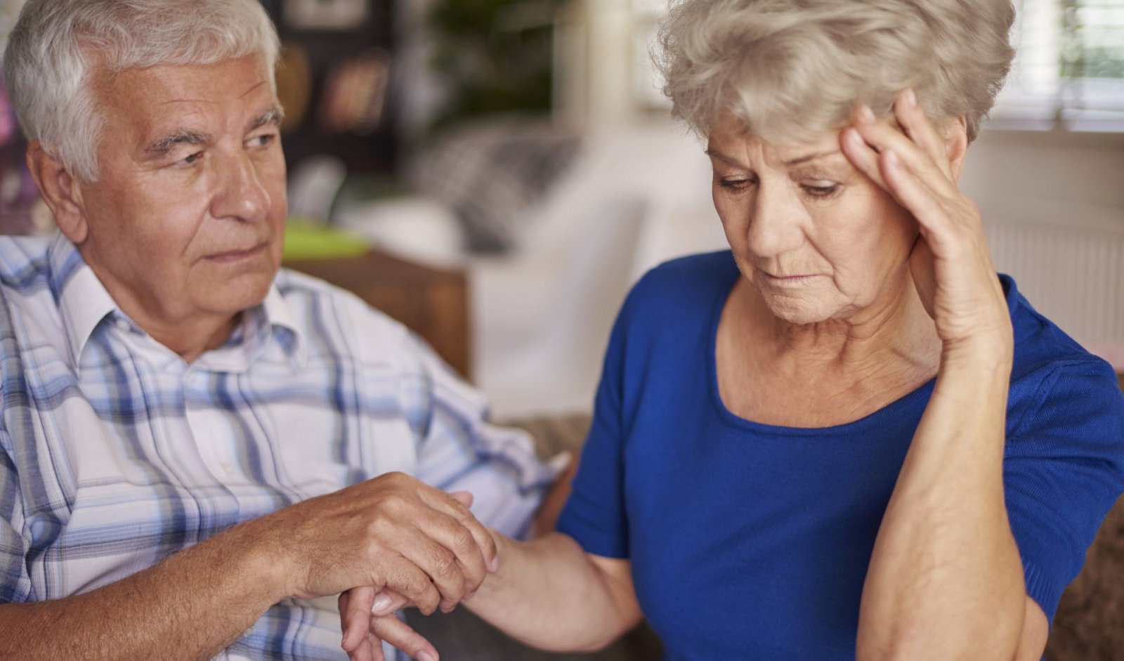 A senior woman holds hands with her husband while looking stressed