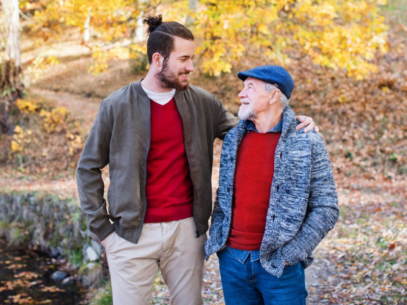 A senior man and his son go for a walk outside on a fall day