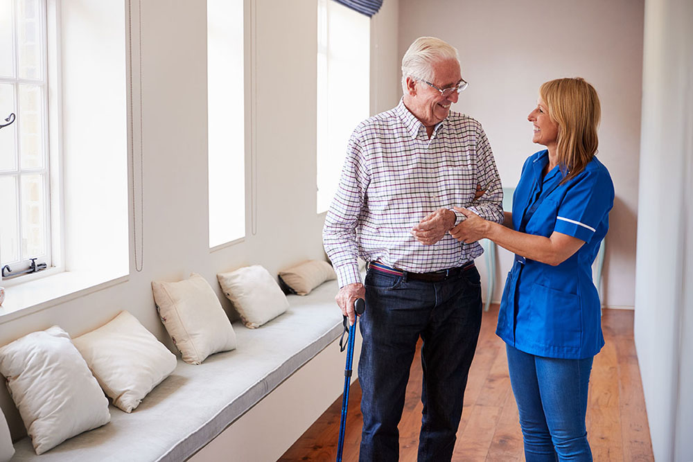 A senior man and his nurse walk down a hallway