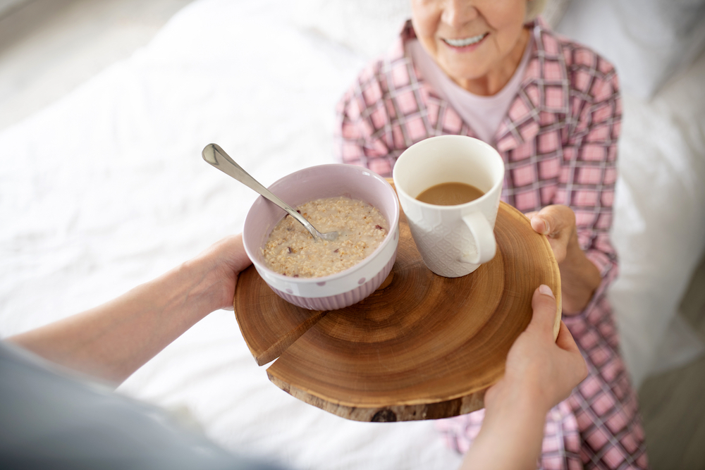 A senior woman being served a bowl of oatmeal and a cup of coffee