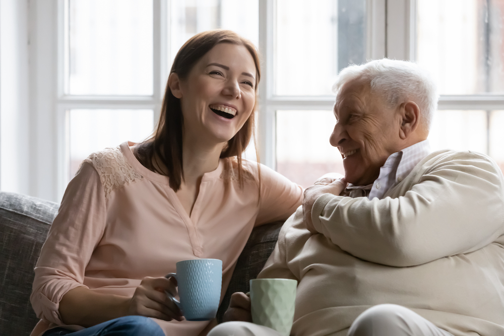 A female caregiver laughs with her senior father
