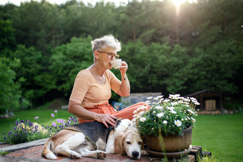 A senior woman enjoys tea while sitting outside with her dog