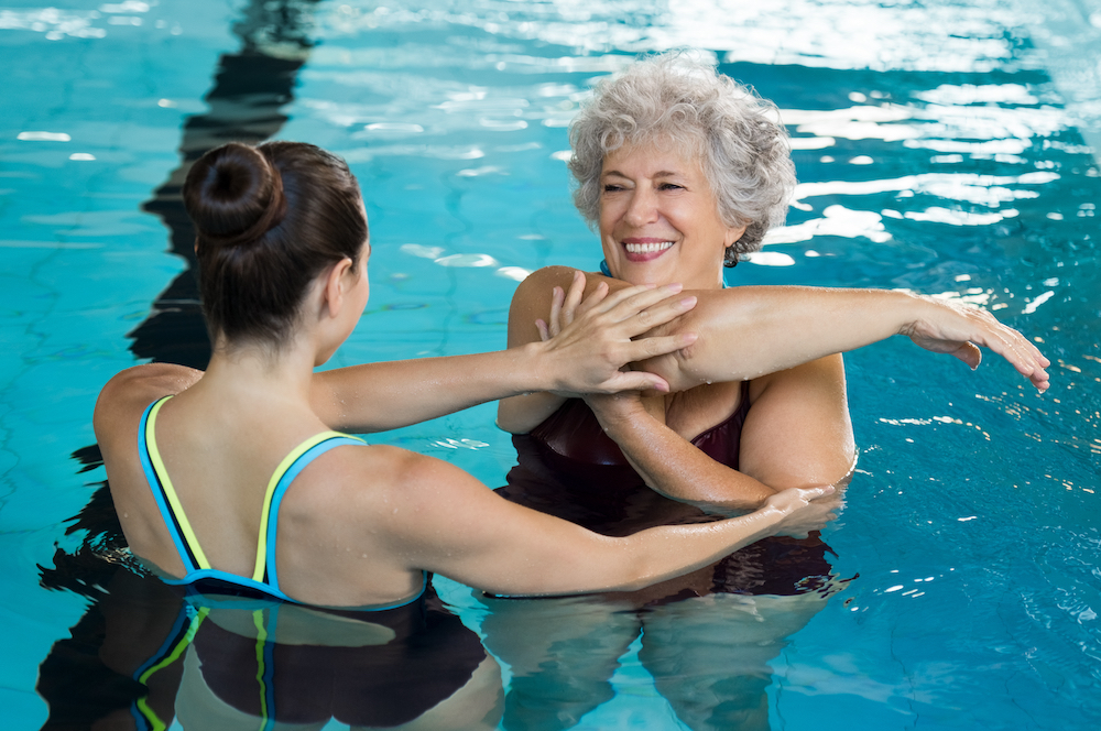 A senior woman stretches in the pool with the help of a trainer