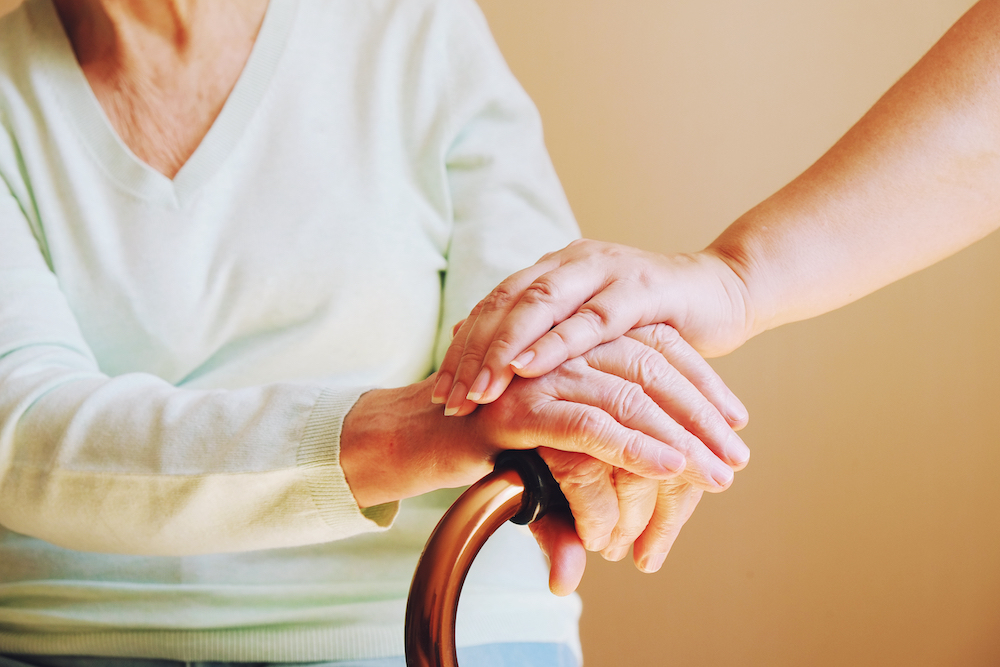 A senior woman holding onto a cane with her caregiver.