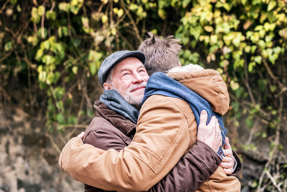 A senior man and his son hug outdoors