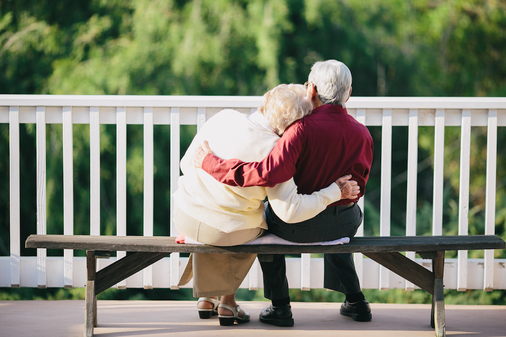 A senior couple hugging and sitting on a park bench