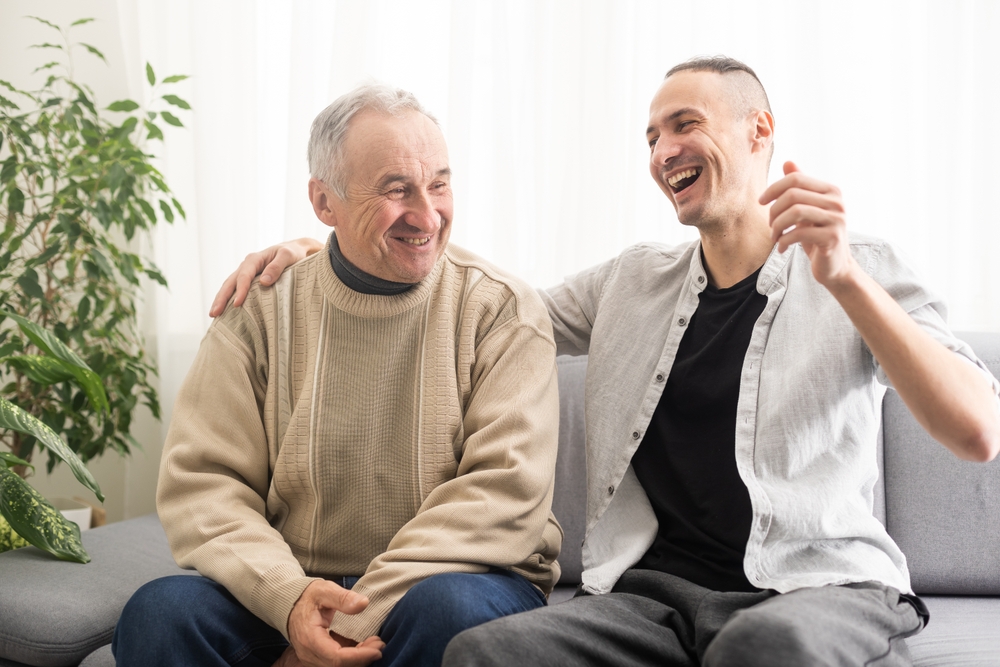 A senior man and young man share a laugh as they enjoy oceanside senior living