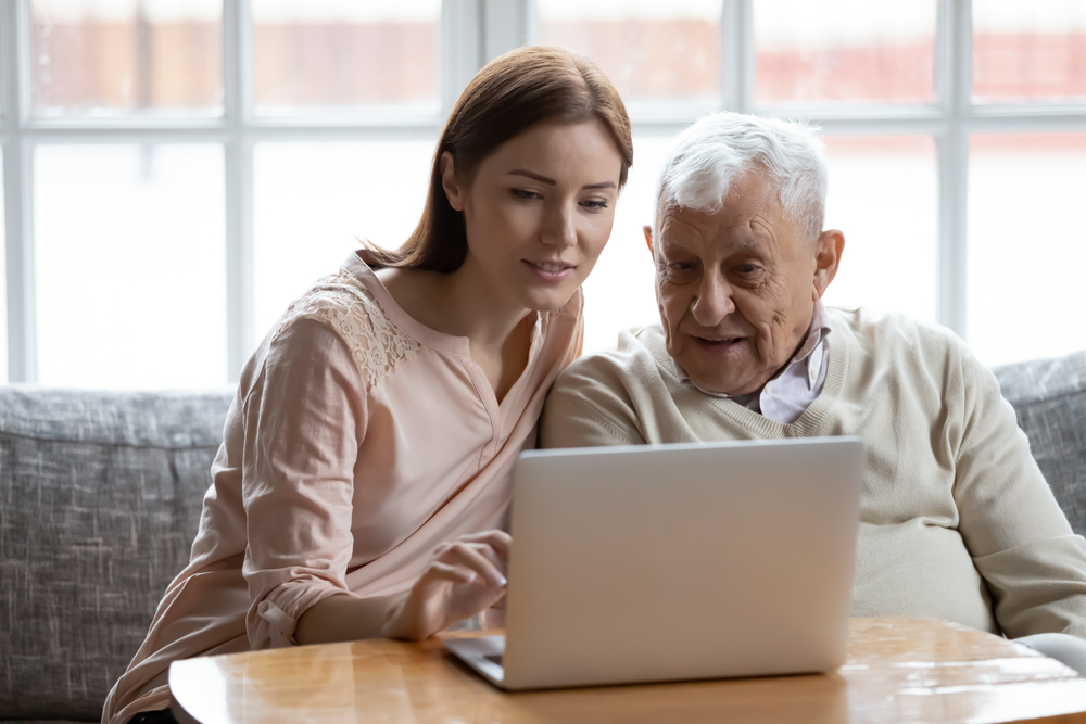 Young woman showing senior man computer skills at oceanside senior living