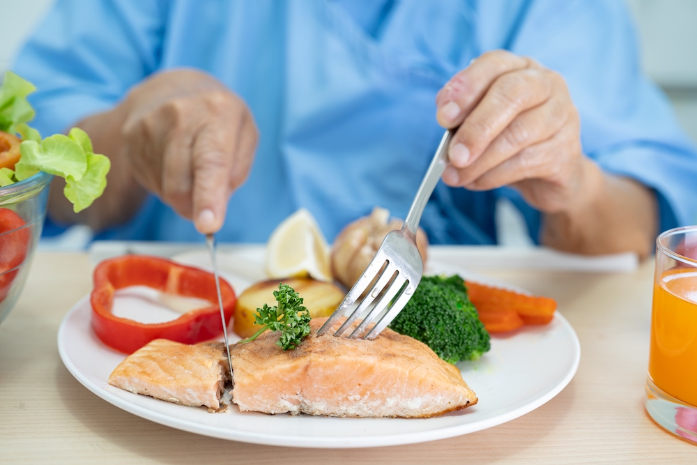 A senior man cutting into a healthy dinner at the memory care community in Oceanside, CA