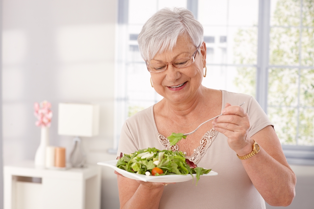 A happy senior woman eating a salad as a part of the dining options offered by Oceanside memory care services